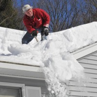 man on top of the roof removing snow