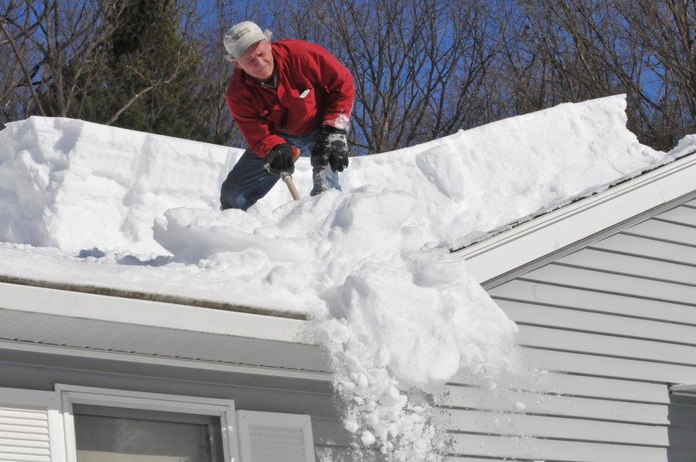man on top of the roof removing snow