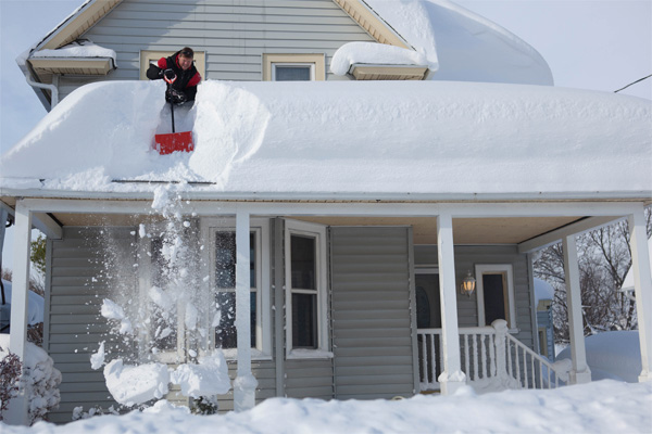 man on top of roof removing snow with a shovel