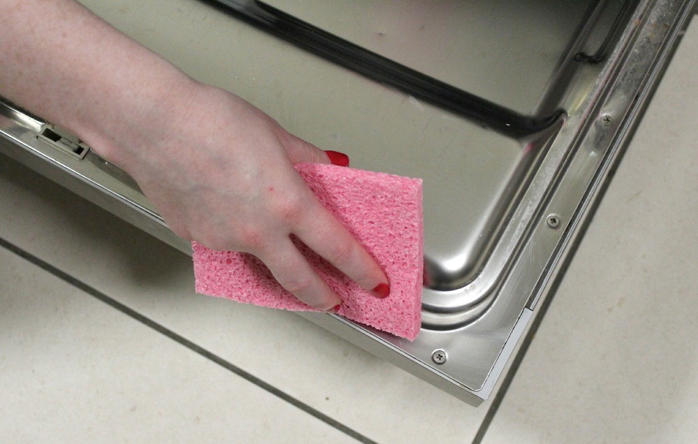 woman cleaning the dishwasher door with a pink sponge
