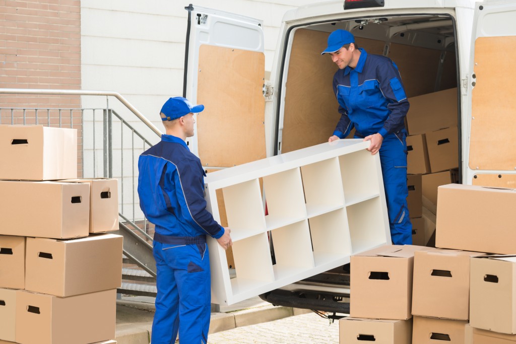 Young male movers unloading furniture and cardboard boxes from truck on street