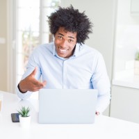 African American business man working using laptop very happy pointing with hand and finger