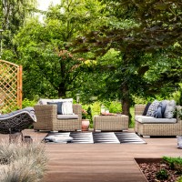 Hanging chair and geometric carpet on wooden patio with garden rattan furniture